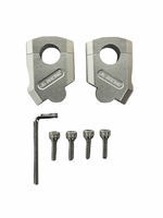 A pair of metallic silver clamp-style parts with a circular cutout, shown above four matching screws and a small hex wrench on a plain white background. The parts appear to be branded with a logo embossed on the front.